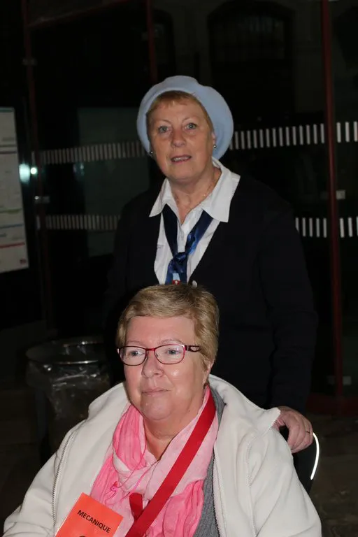 Une hospitalière en béret penchée vers une pèlerine assise
